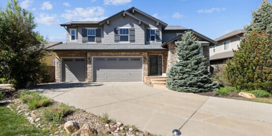 Two-story modern craftsman home with a stone and gray siding exterior, featuring a three-car garage, manicured landscaping, and a large concrete driveway